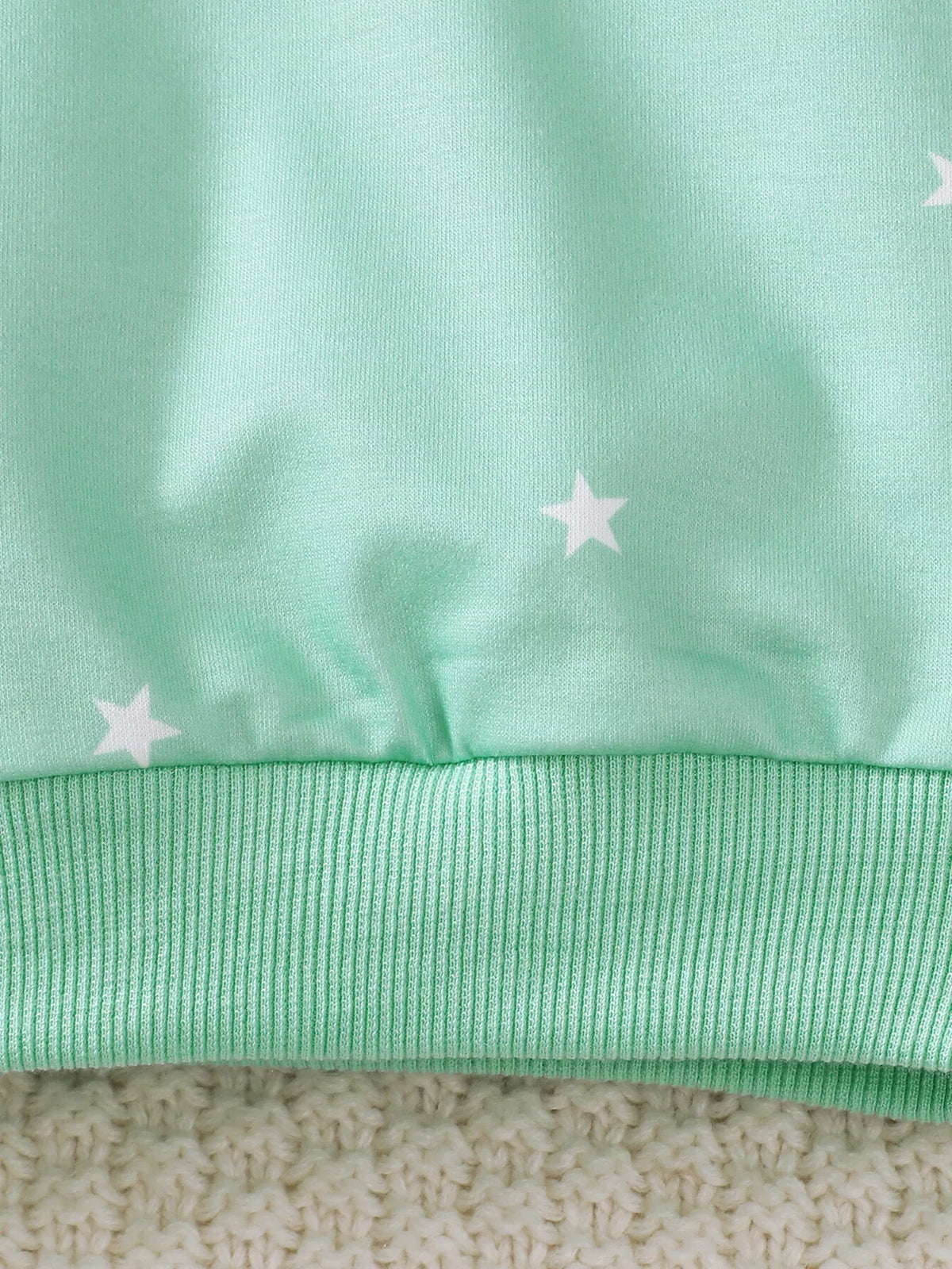 Close-up of the mint sweatshirt's white stars and ribbed hem.