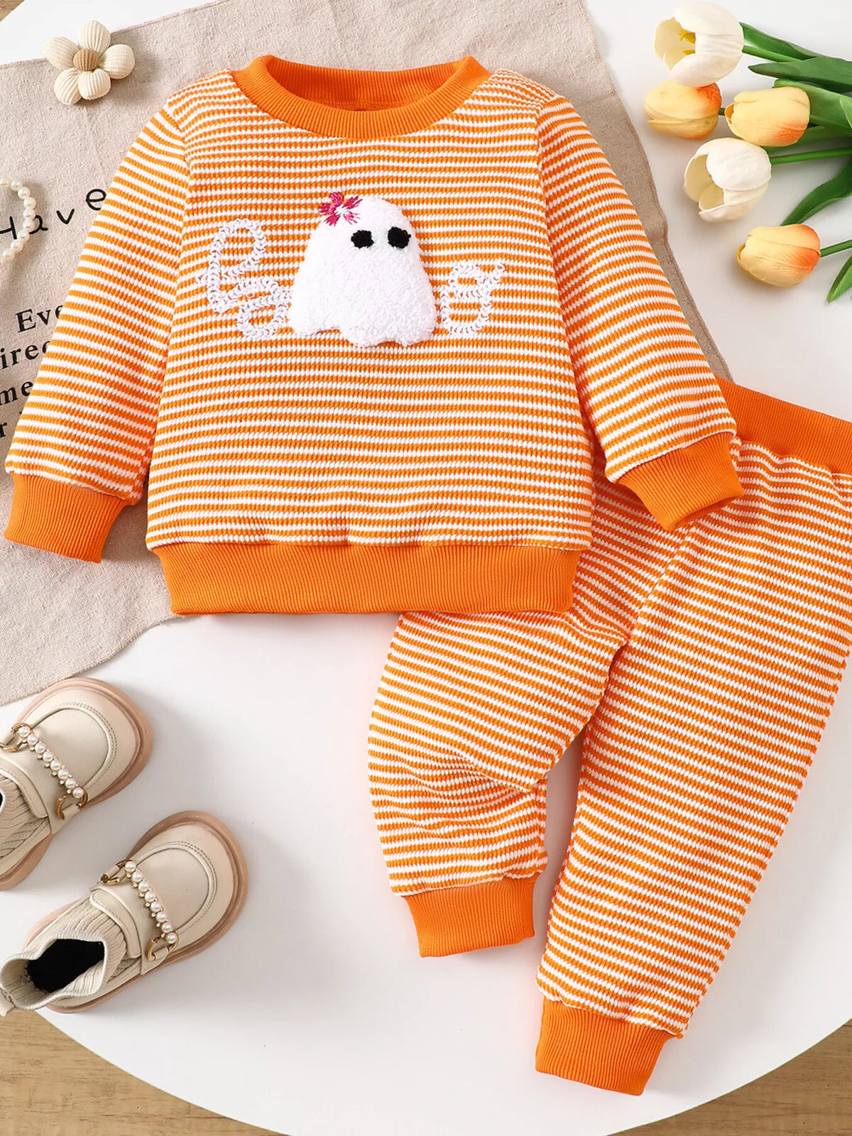 Orange striped ghost graphic pajama top and matching pants displayed flat