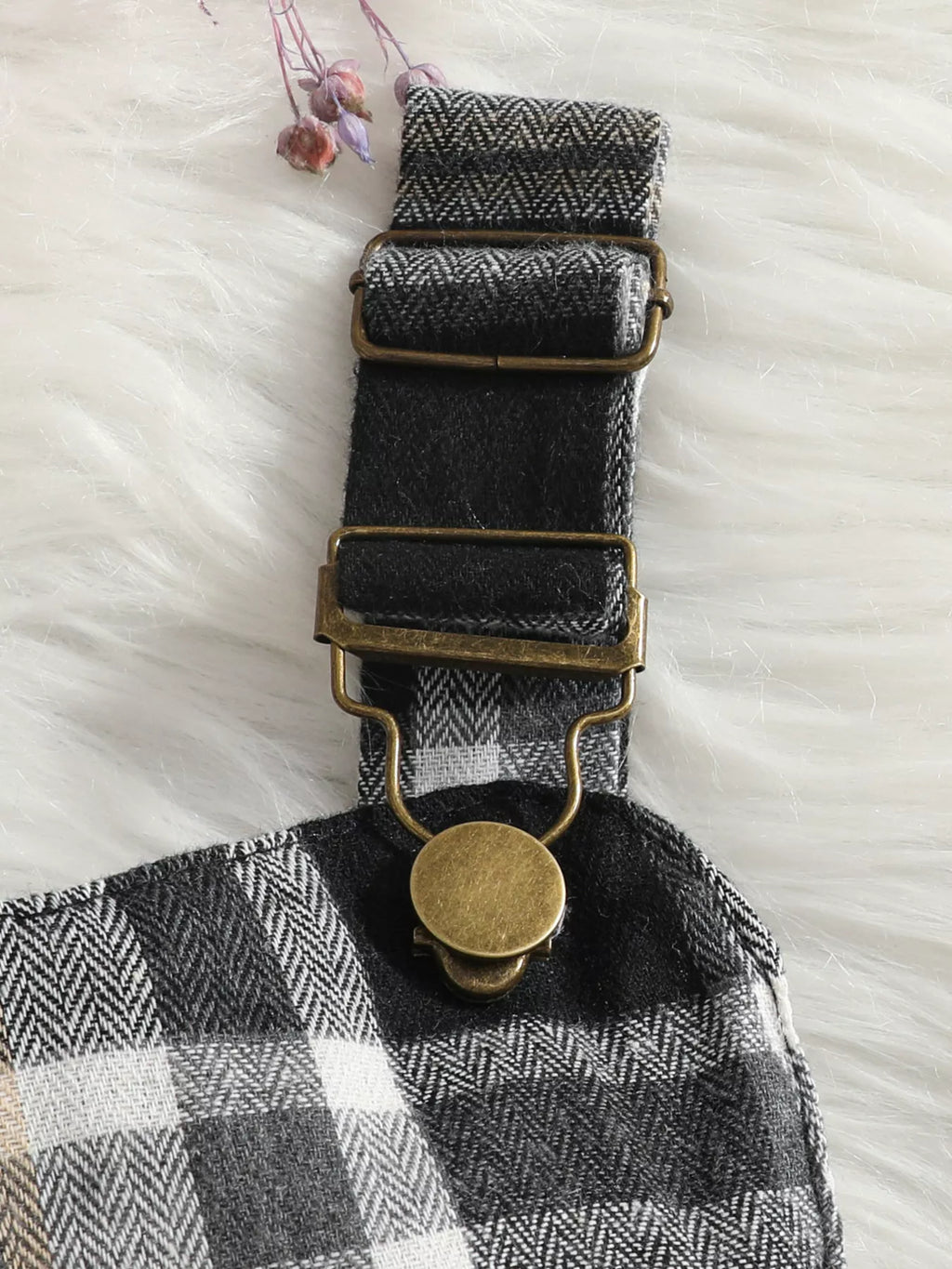 Close-up of a dark suspender strap buckle and button on the black-and-white plaid skirt.
