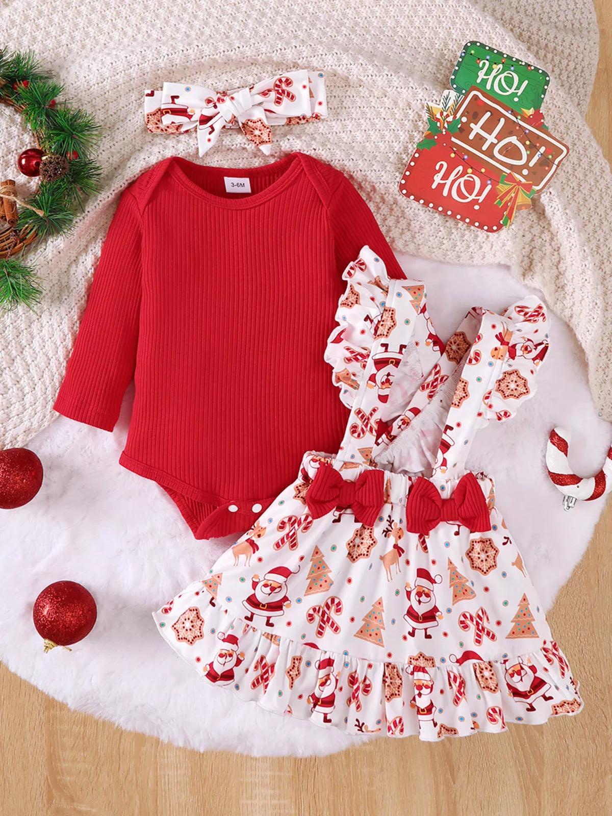 Flat lay of a red baby bodysuit, Santa-print suspender skirt and matching bow headband.