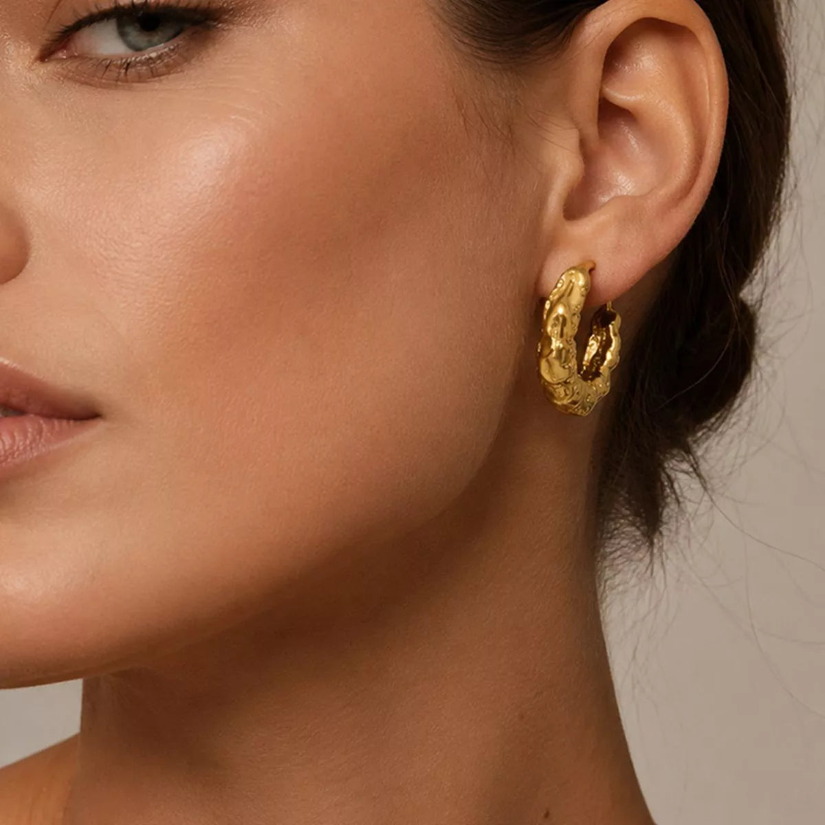 Textured gold-tone hoop earrings worn on a model