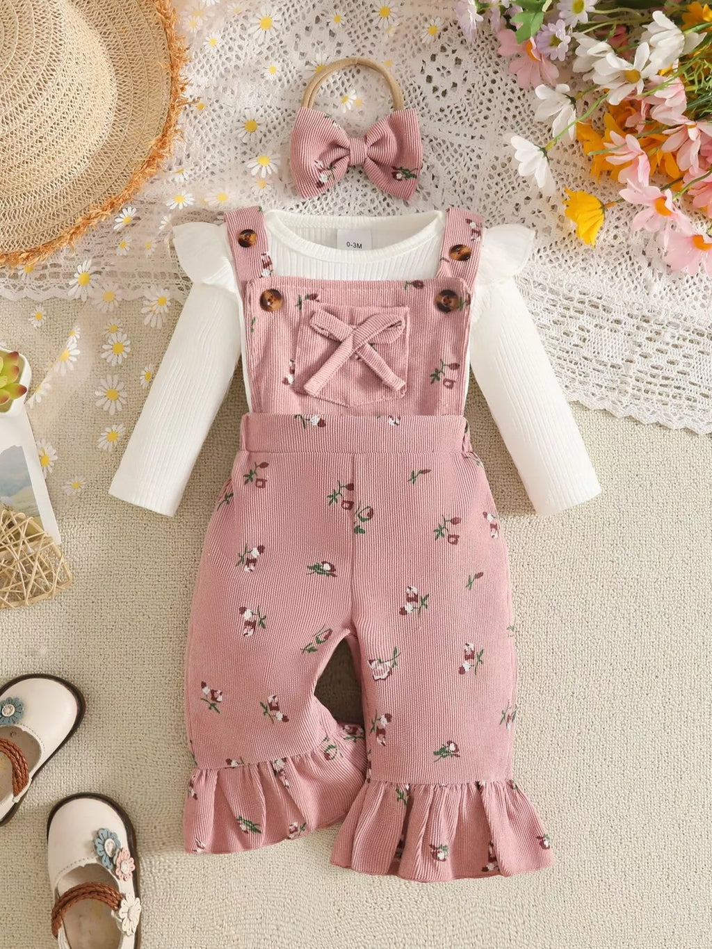 White ribbed baby bodysuit with pink bow-accented overalls and matching headband displayed flat