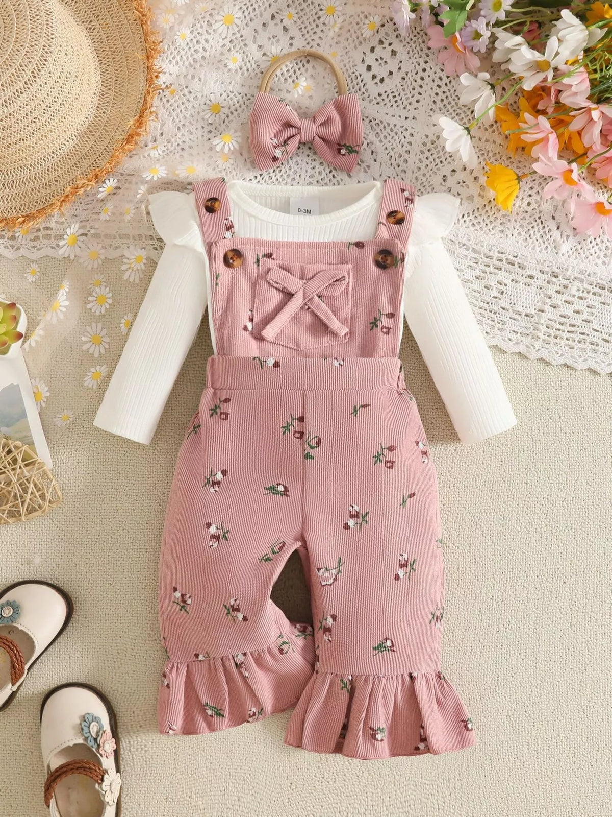White ribbed baby bodysuit with pink bow-accented overalls and matching headband displayed flat