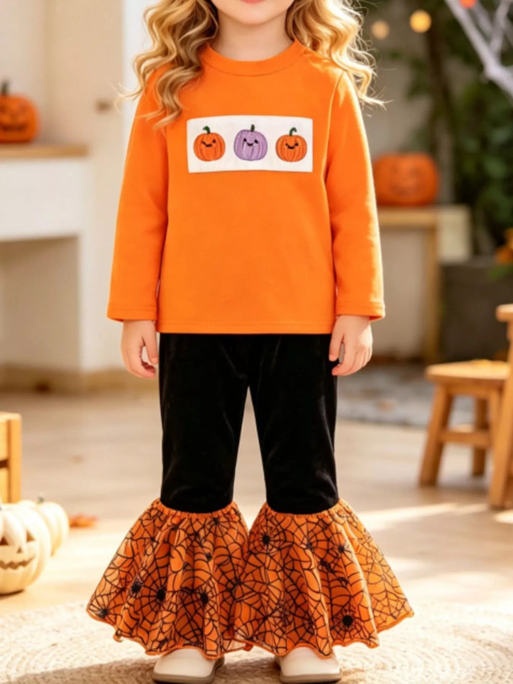 Child wearing an orange pumpkin graphic top and black pants with orange patterned flared hems.