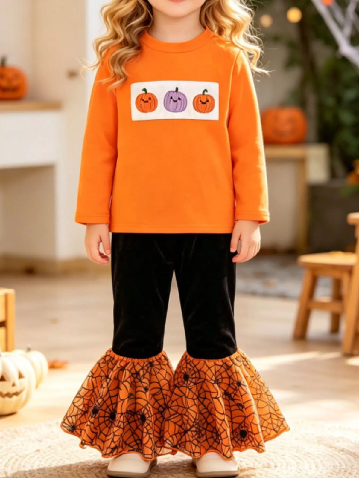 Child wearing an orange pumpkin graphic top and black pants with orange patterned flared hems.