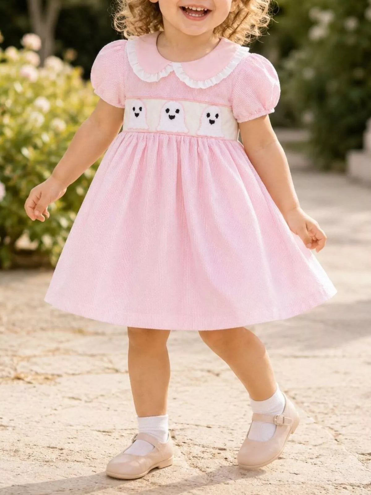 Child wearing a pink puff-sleeve dress with white collar and ghost-print waistband.
