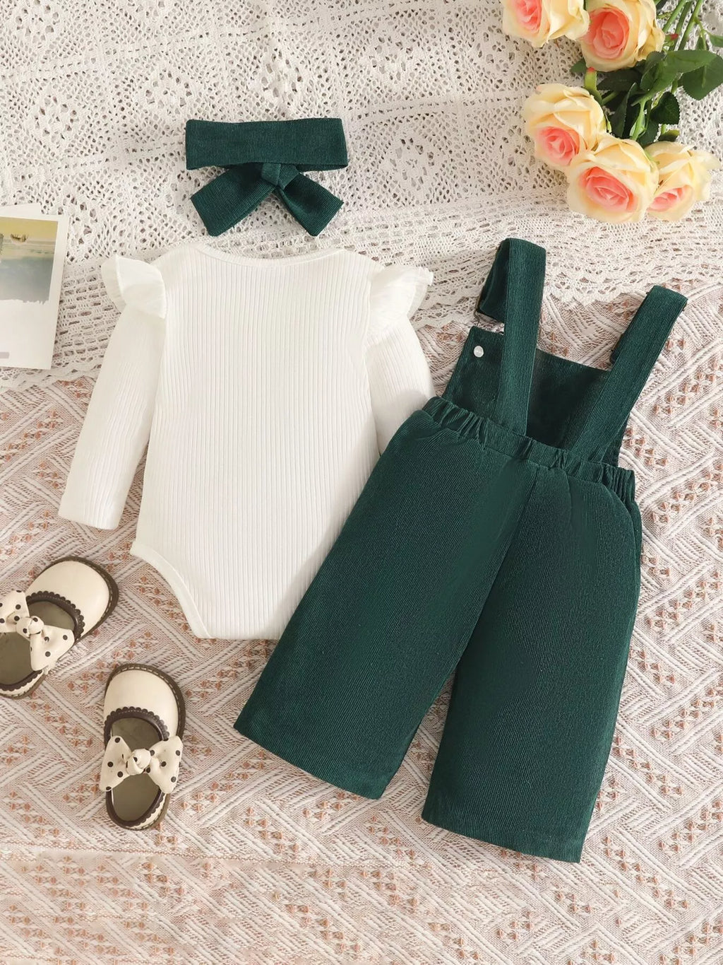 White ribbed baby bodysuit with dark green bow-embroidered overalls and matching headband displayed flat