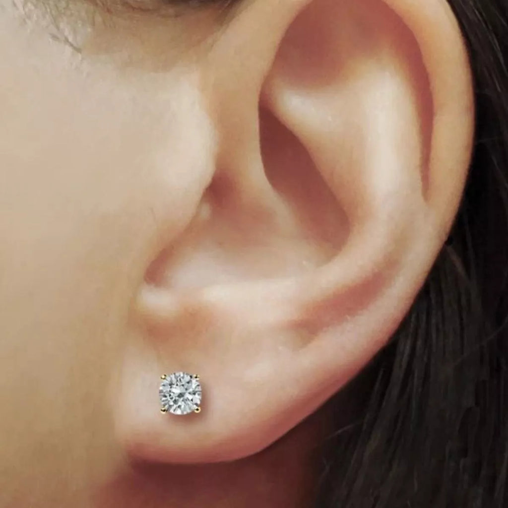Gold-tone stud earrings with round clear stones worn on a model