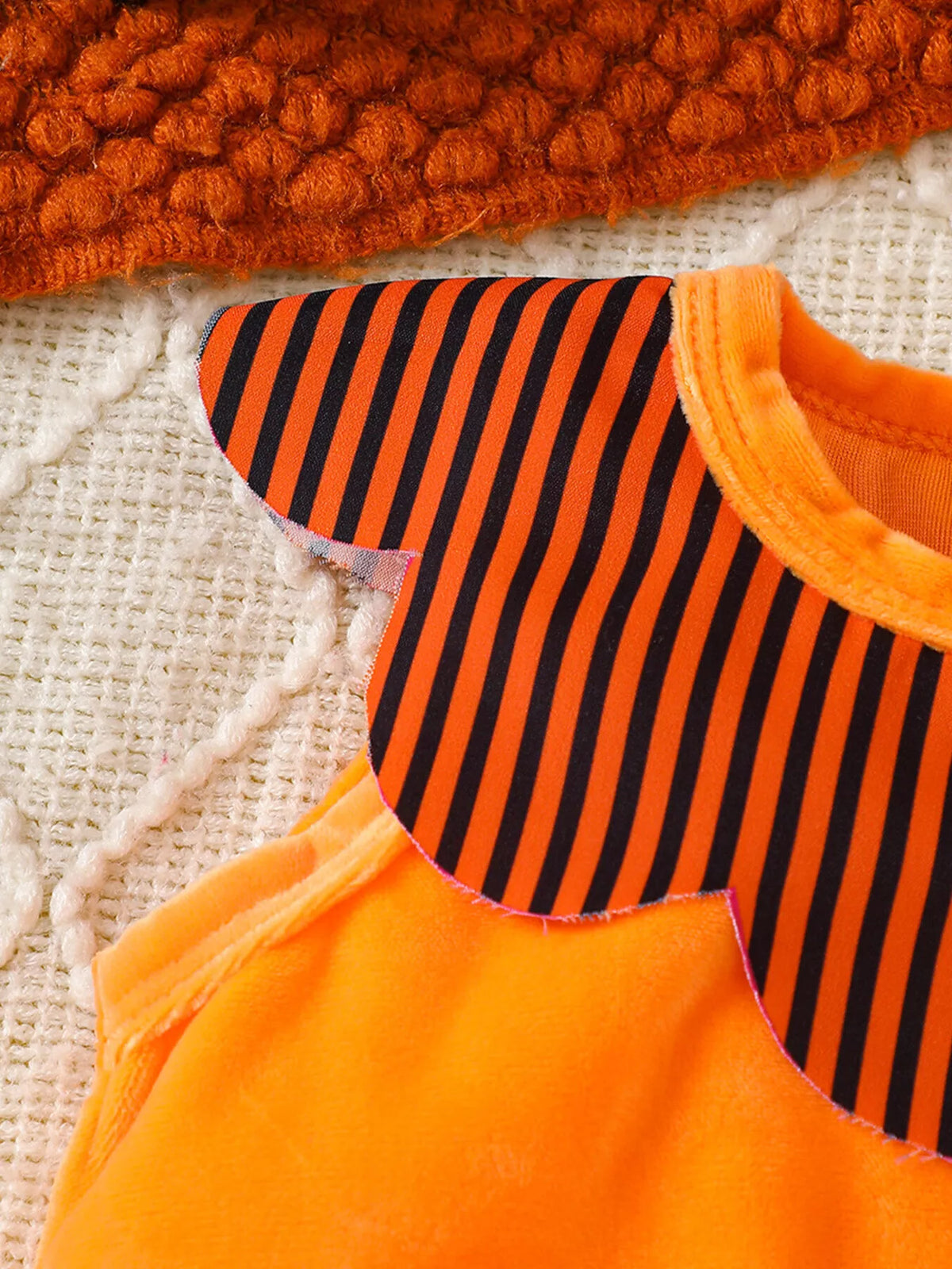 Orange arm opening and striped yoke detail of the baby bodysuit