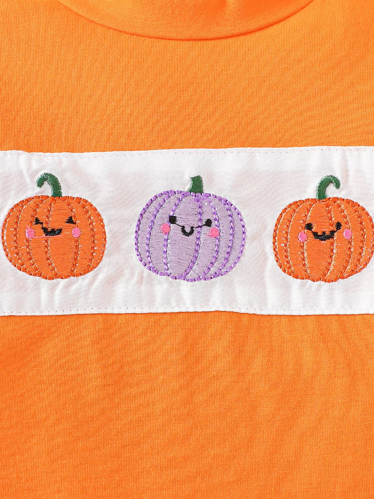 Close-up of the orange top's three smiling pumpkin graphics in a white chest panel.