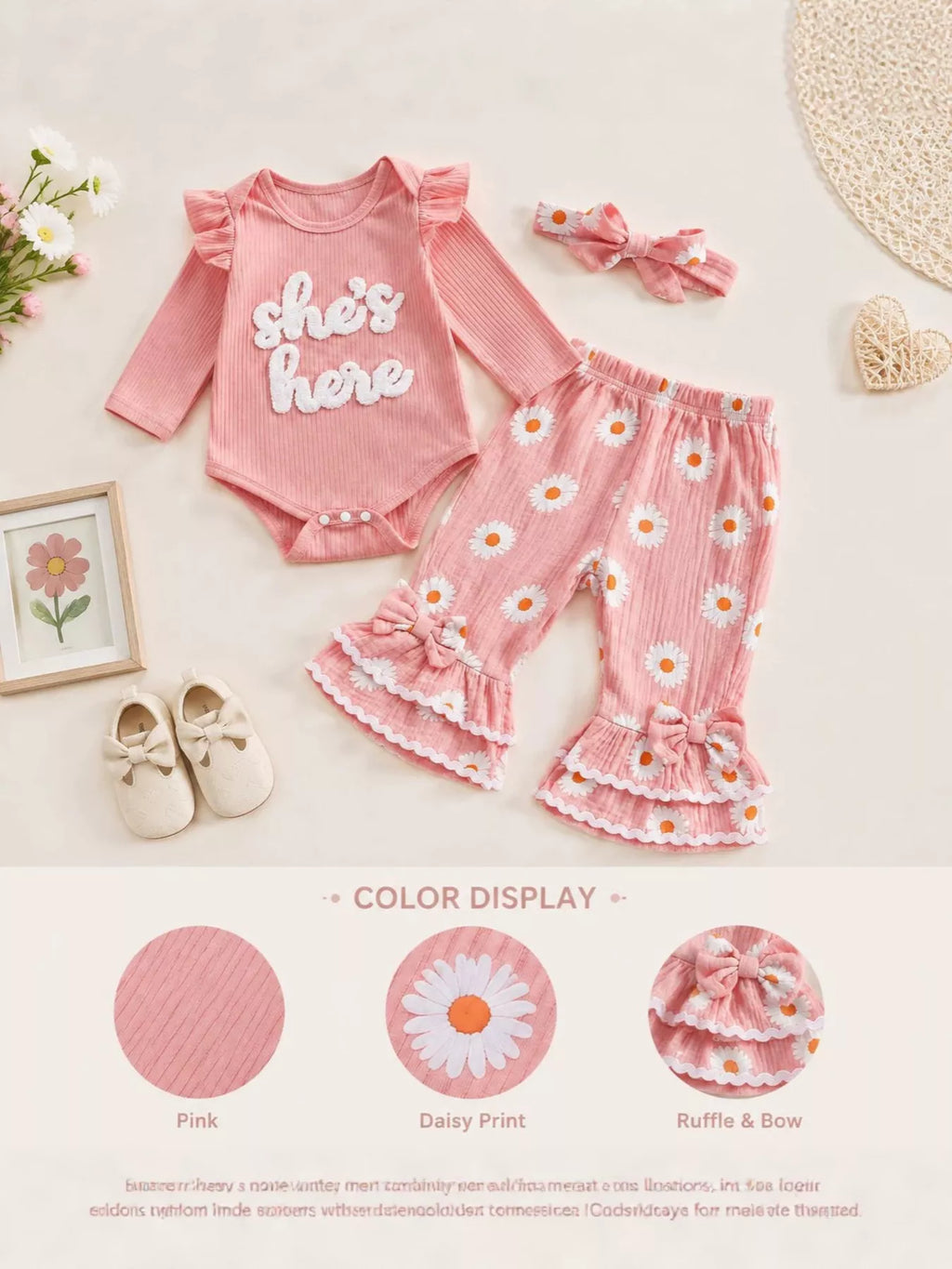 Pink She's Here baby outfit with daisy-print ruffle pants and headband on a product display.