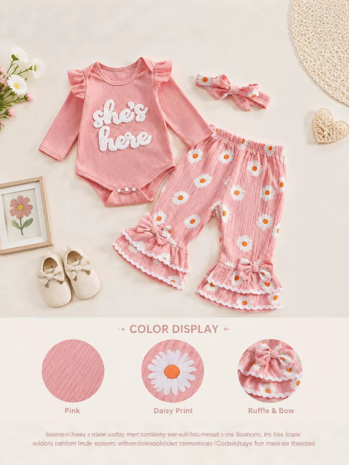 Pink She's Here baby outfit with daisy-print ruffle pants and headband on a product display.