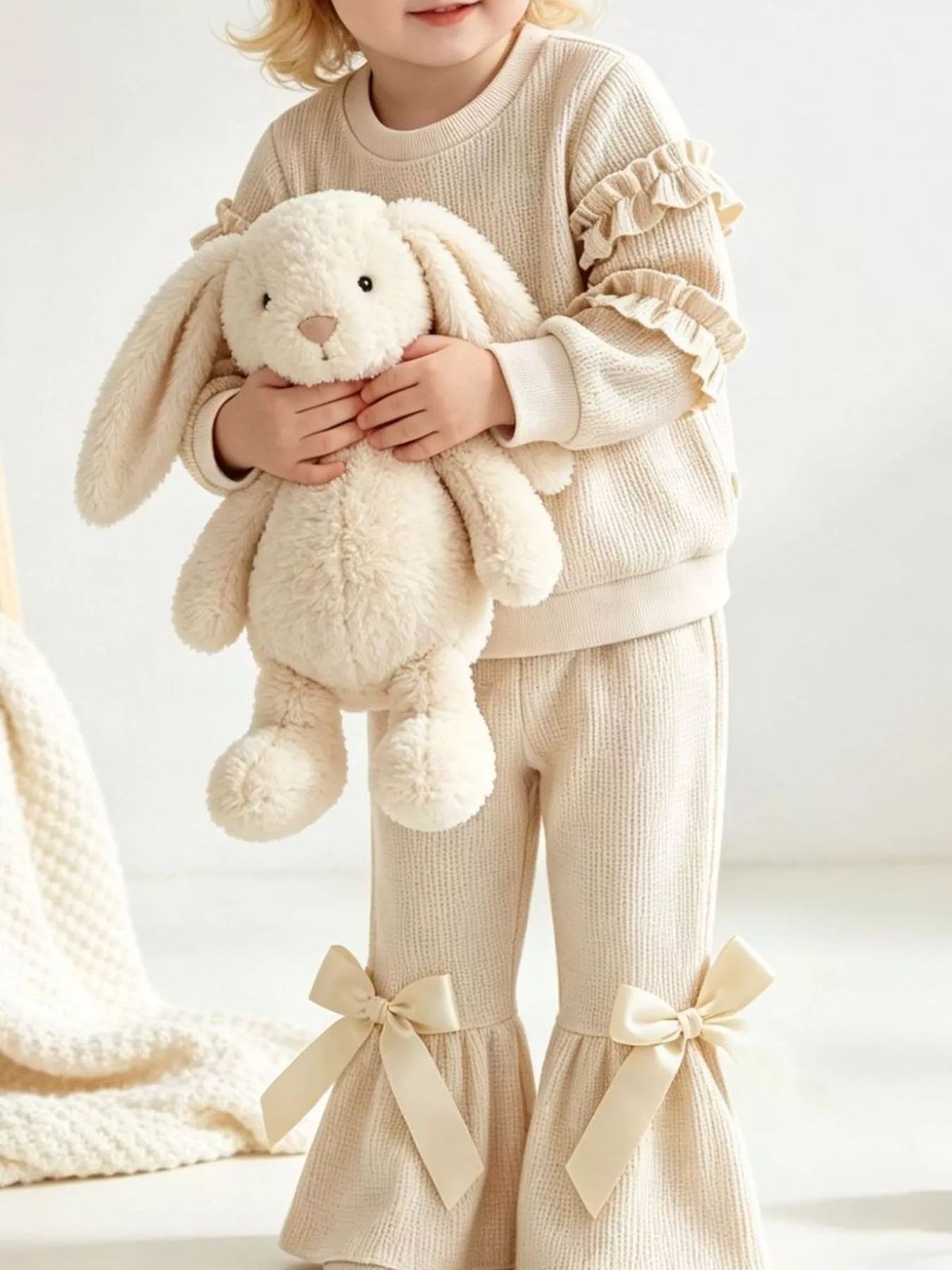 Cream ruffle-sleeve sweatshirt and bow-accented flared pants worn by a child