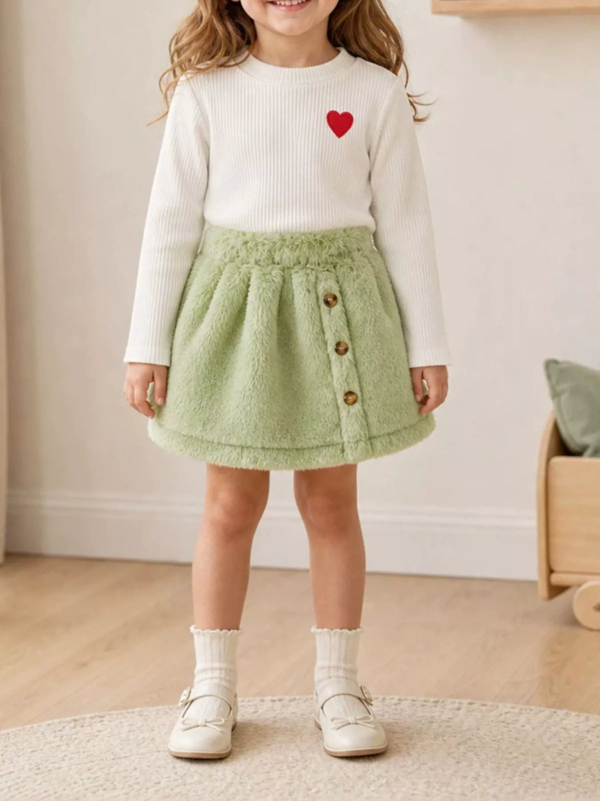 White heart-embroidered top and green fuzzy skirt worn by a child