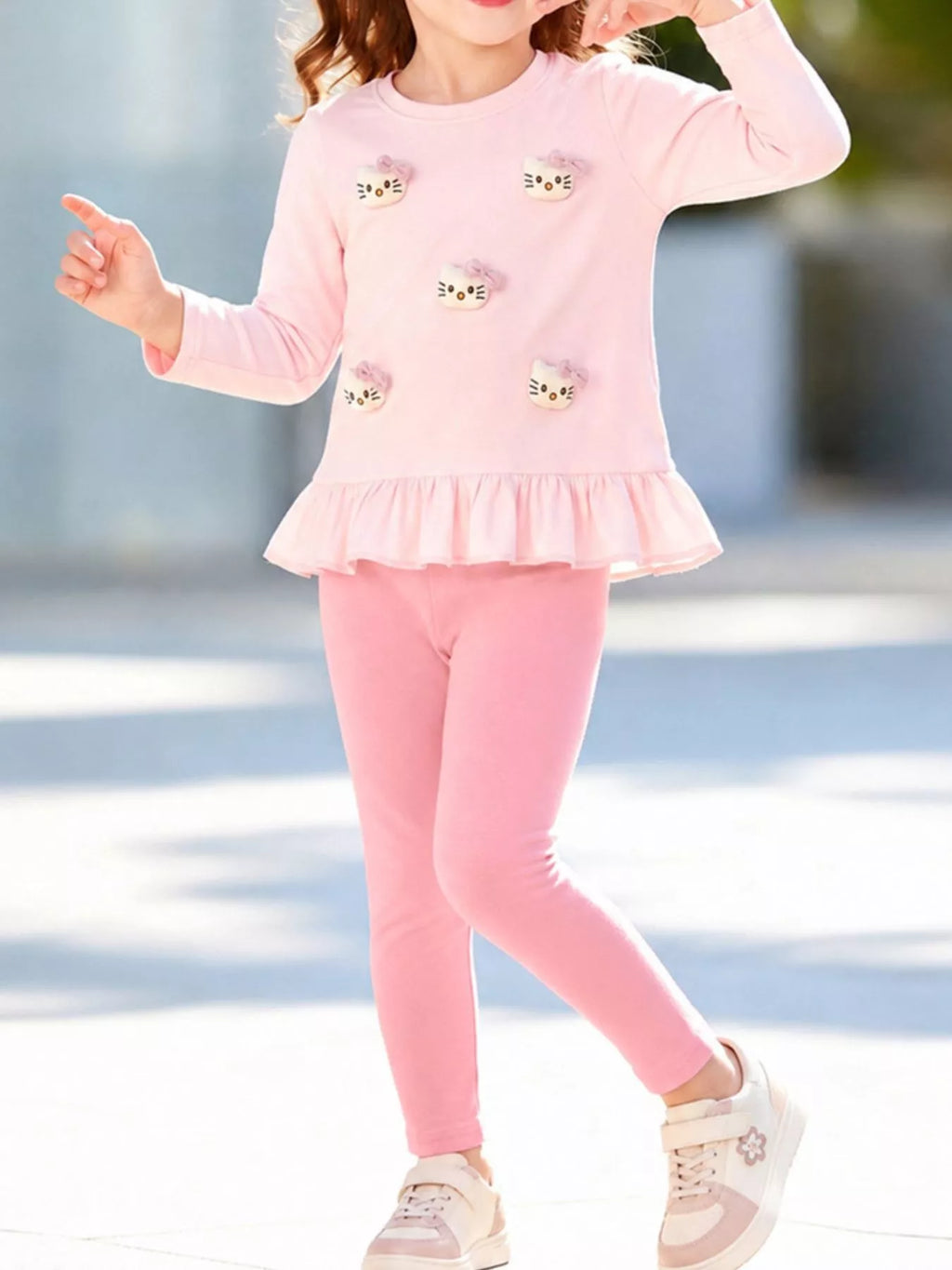 Child wearing the pink cat-applique peplum top and pink leggings outdoors.