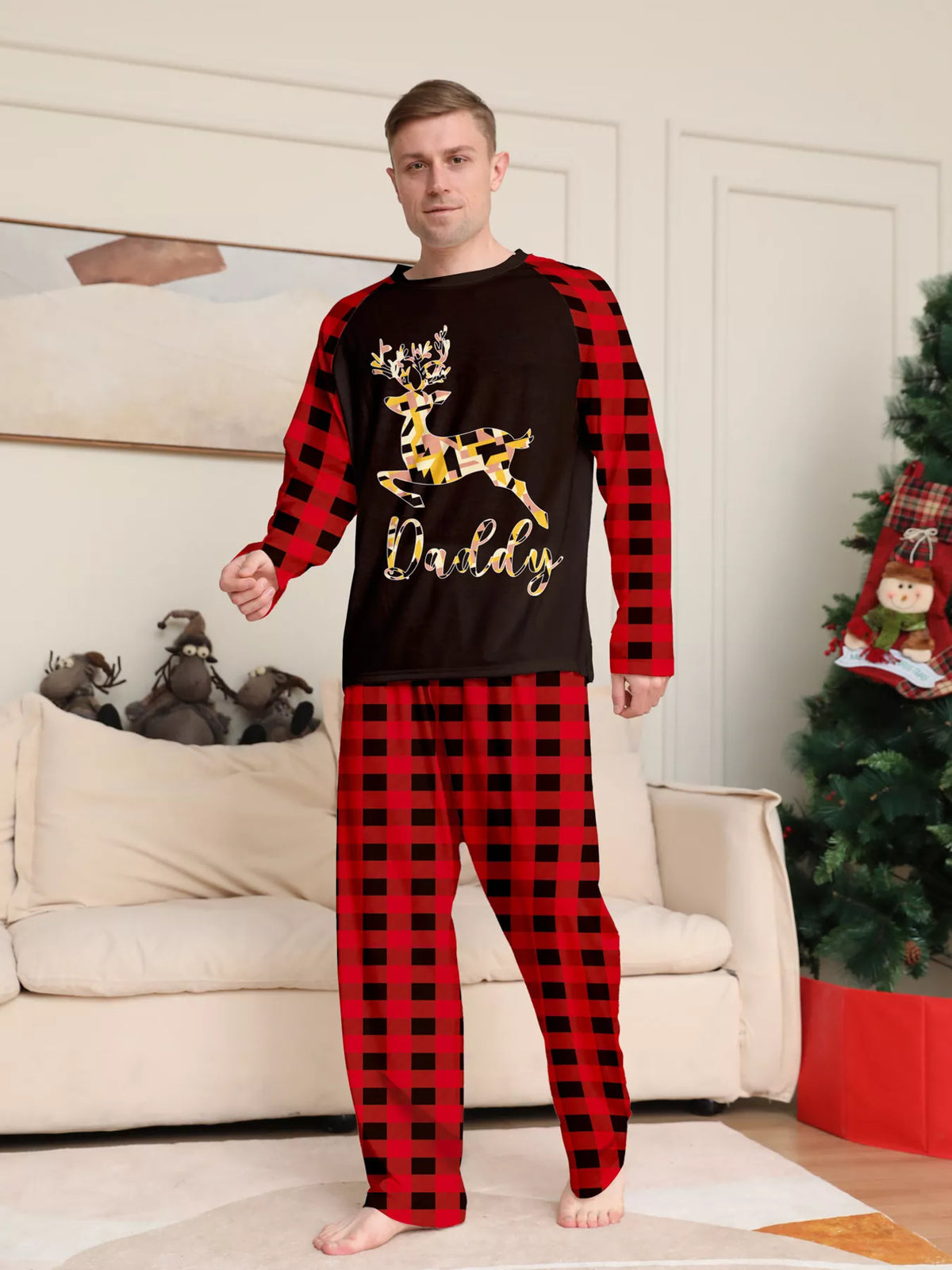 Man modeling a black gold-tone reindeer graphic pajama top with red plaid sleeves and matching pants.