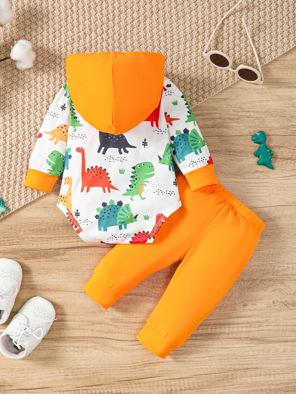 Children’s white dinosaur-print hooded bodysuit and orange pants displayed flat