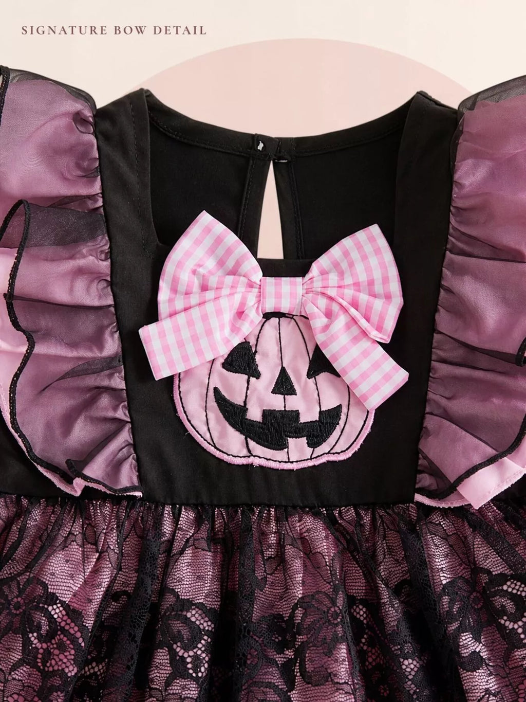Close-up of the pink pumpkin applique and gingham bow on the black dress bodice.