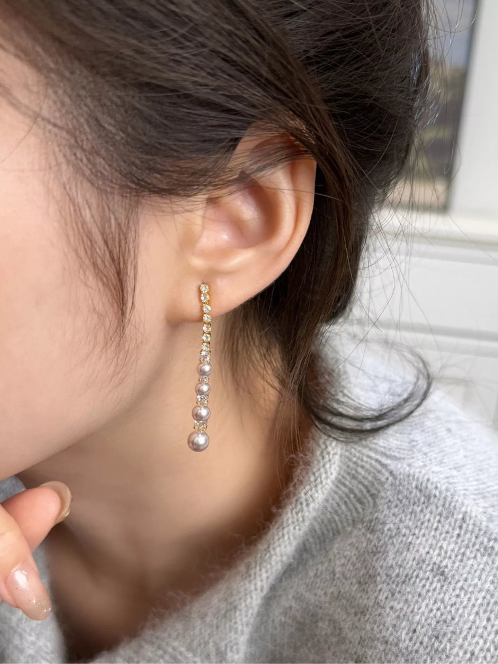 Gold-tone long pearl-like bead and clear stone drop earrings worn on a model