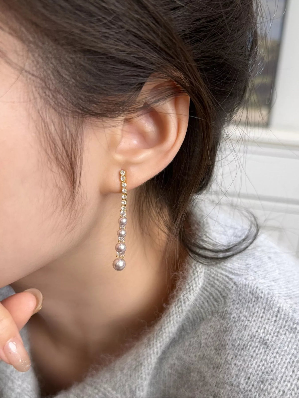 Gold-tone long pearl-like bead and clear stone drop earrings worn on a model
