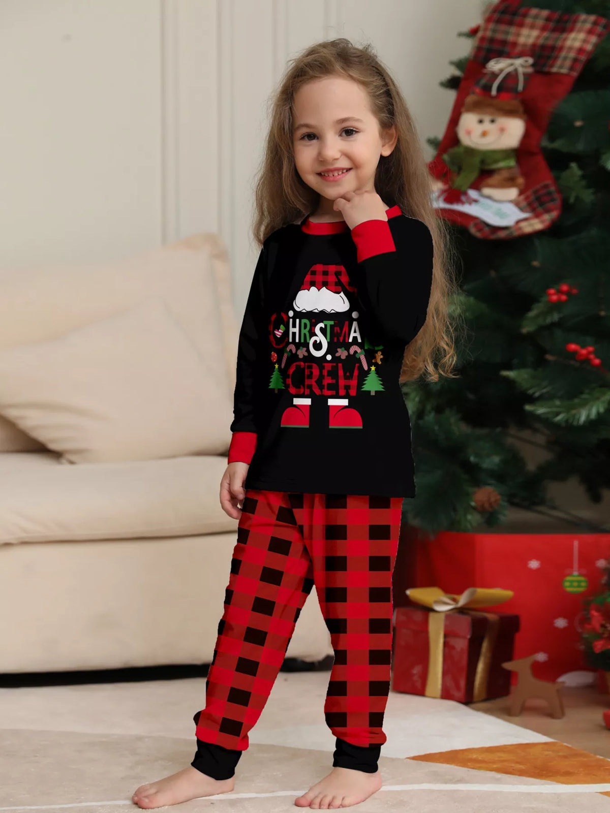 Child wearing the black Christmas graphic pajama top with red cuffs and plaid pants.