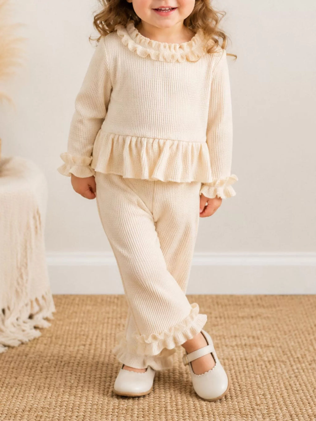 Front view of a child wearing the cream ruffle-trim two-piece outfit.