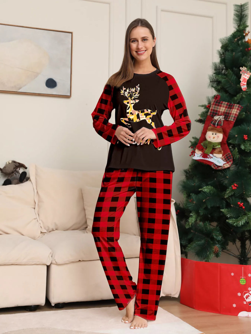 Woman modeling a black gold-tone reindeer graphic pajama top with red plaid sleeves and matching pants.