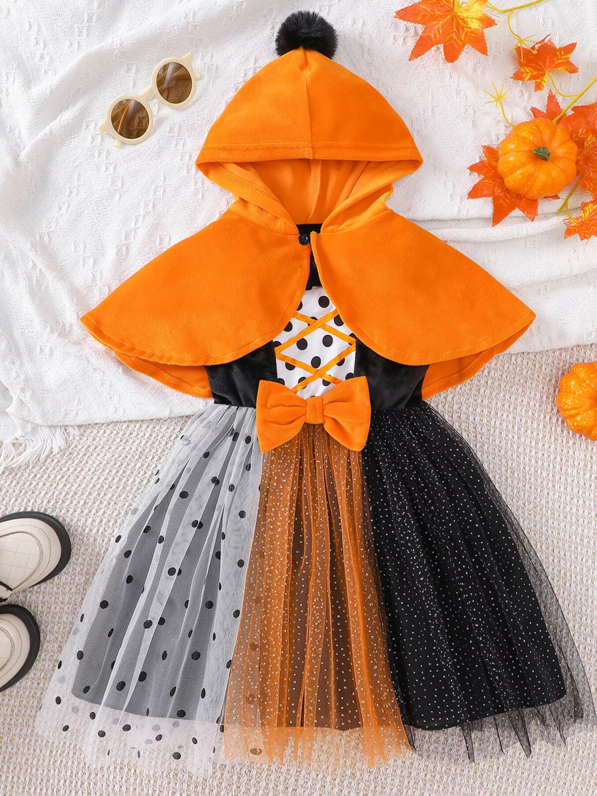 Front view of the orange cape and black dress with lace-up polka-dot panel and multicolor tulle skirt.