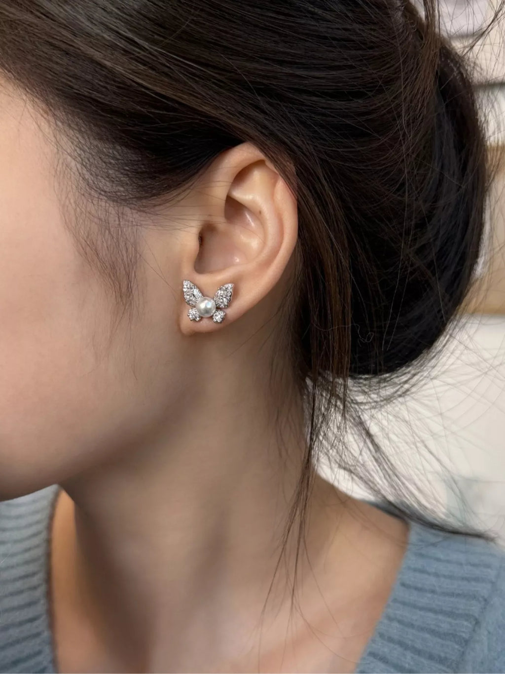 Butterfly-shaped pearl-like bead and clear stone stud earrings worn on a model