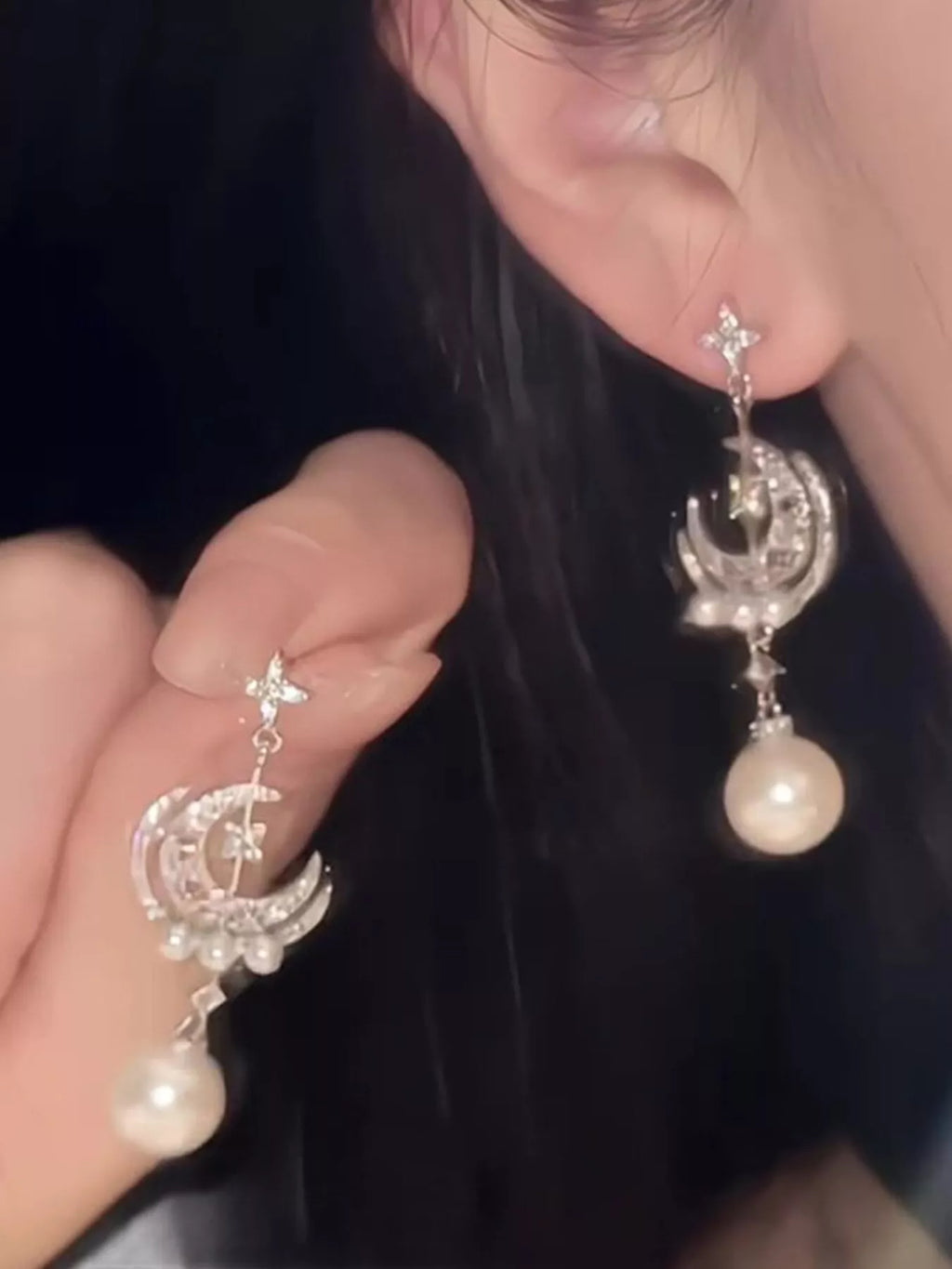 Moon and star dangle earrings with pearl-like bead drops worn on a model