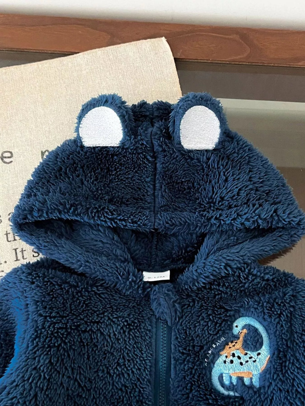 Navy fleece hood with rounded ears and a small dinosaur chest graphic