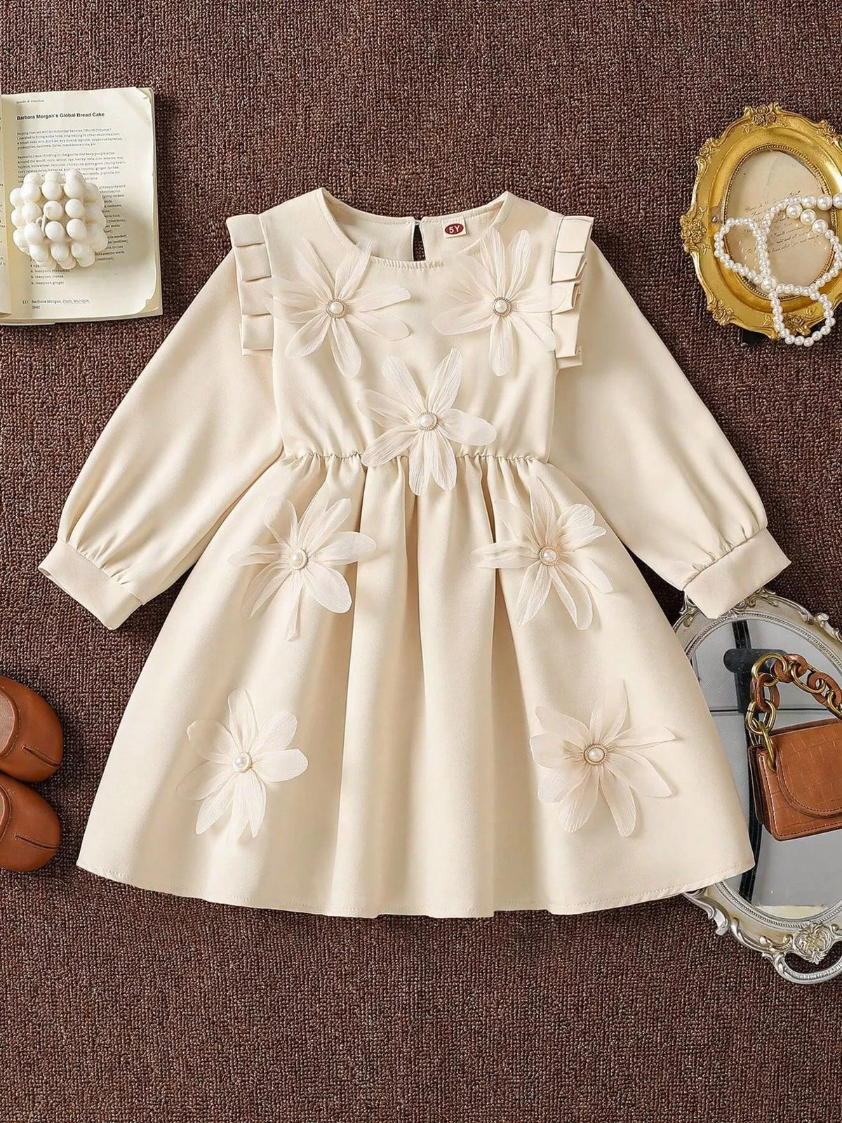Flat lay of a cream long-sleeve dress with floral appliques and a gathered skirt.
