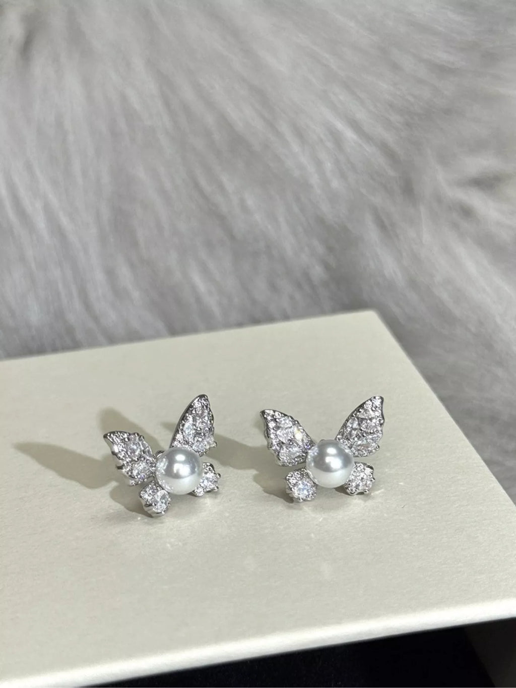 Butterfly-shaped pearl-like bead and clear stone stud earrings — detail view