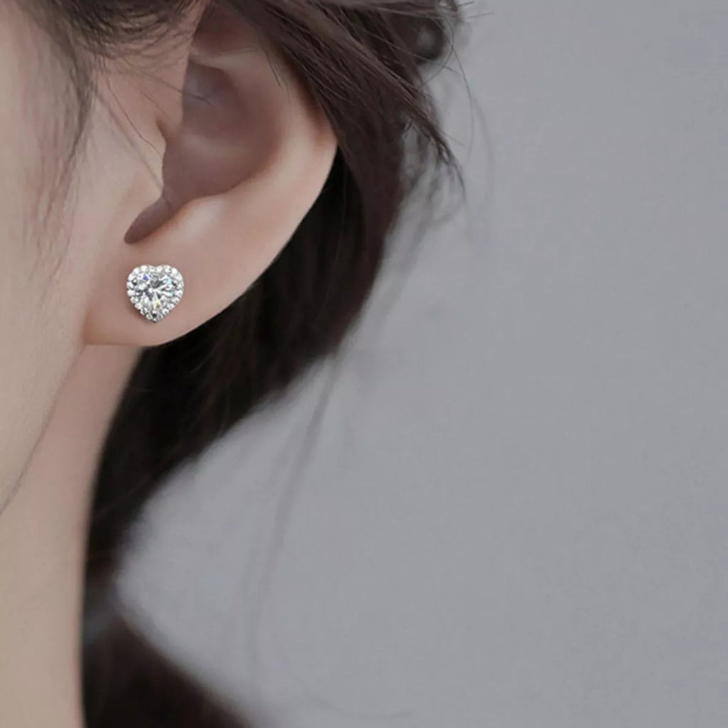 Heart-shaped clear stone halo stud earrings worn on a model