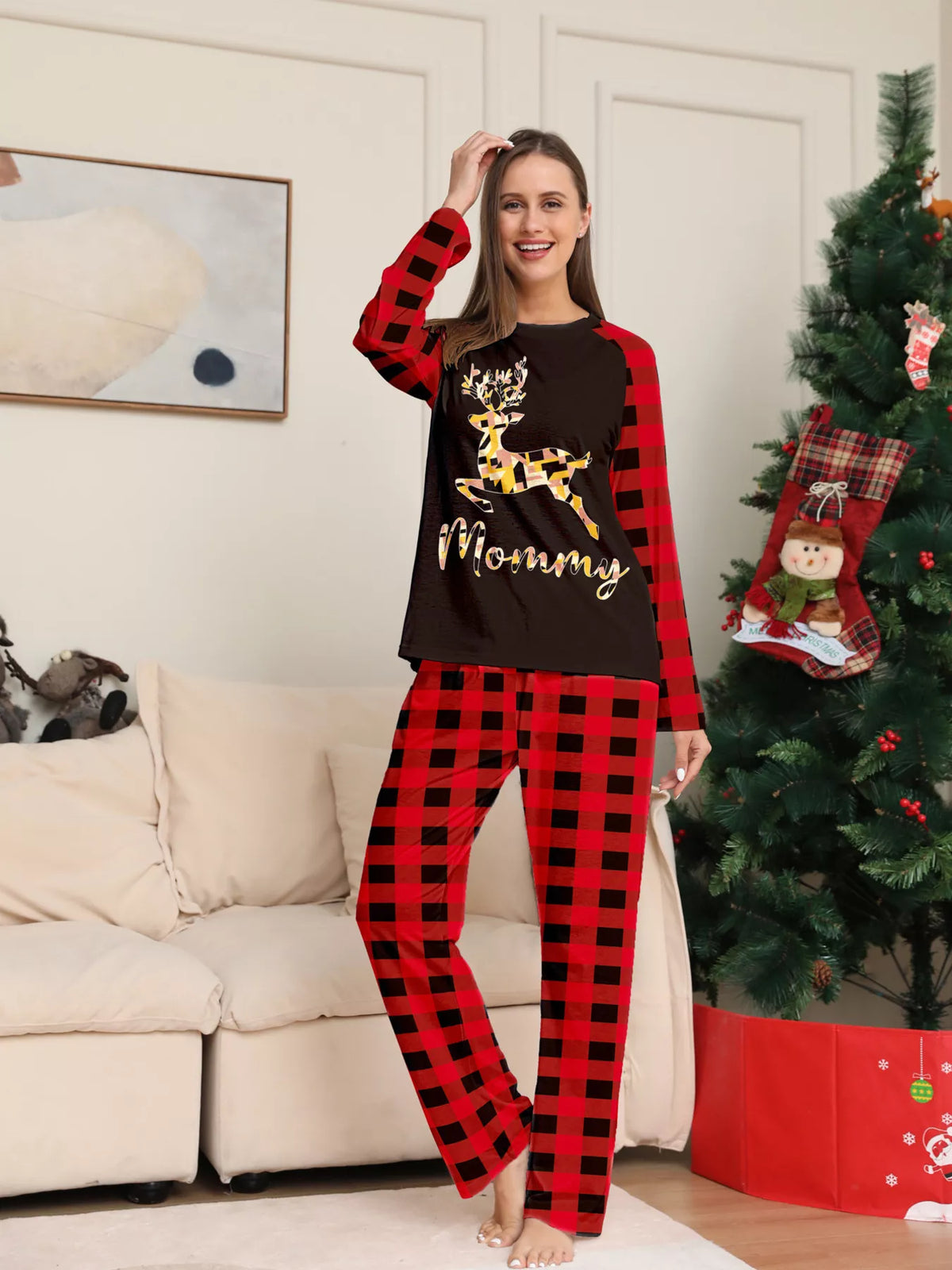 Woman modeling a black gold-tone reindeer graphic pajama top with red plaid sleeves and matching pants.