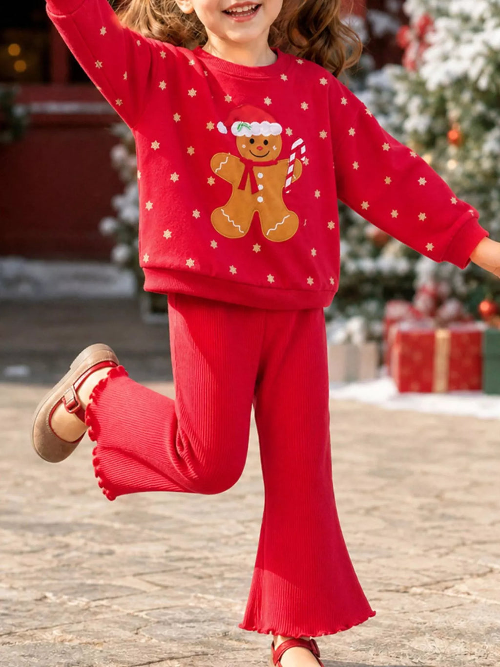 Child wearing a red gingerbread graphic sweatshirt with matching red flared pants.