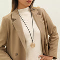 Long black cord necklace with a round gold-tone spiral pendant — detail view