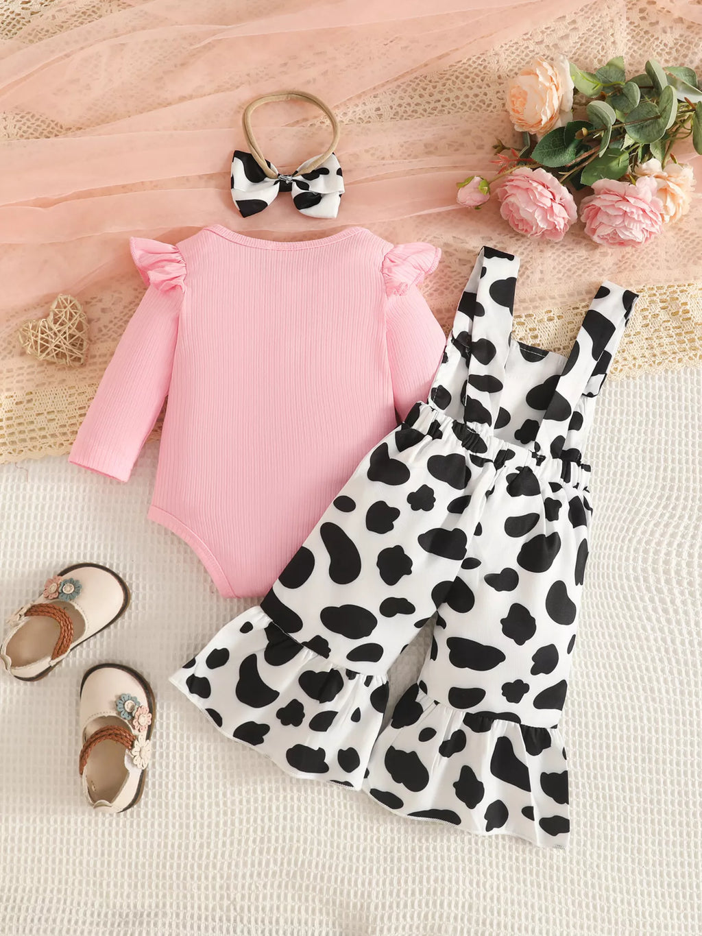 Back flat lay of the pink bodysuit, cow-print flared overalls and matching bow.