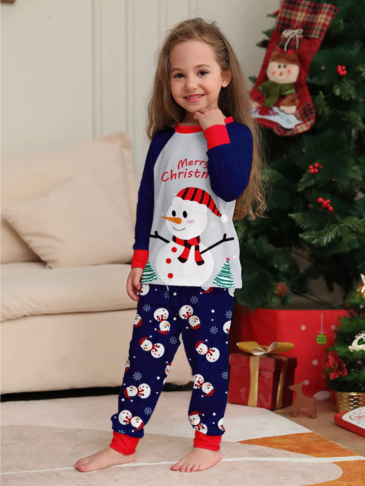 Child wearing a white Merry Christmas snowman top and navy printed pajama pants.