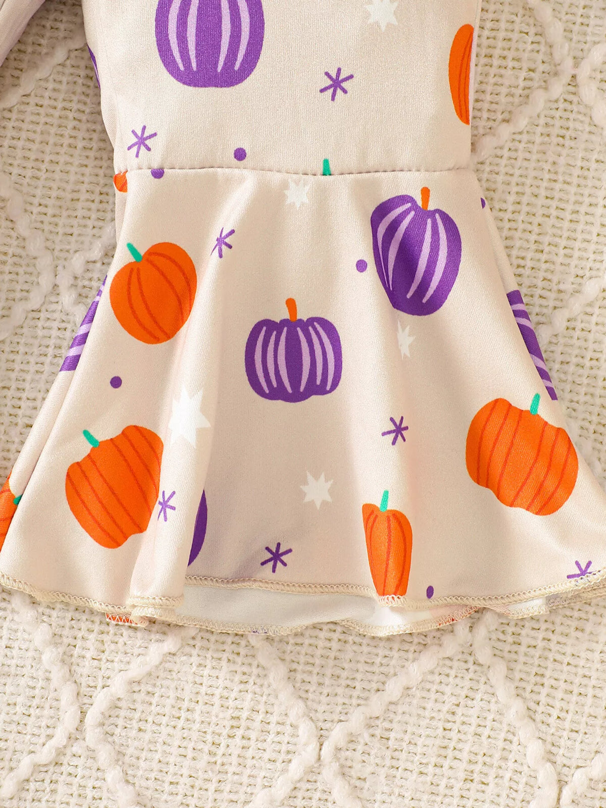 Close-up of the cream pumpkin-print overalls' flared leg hem.