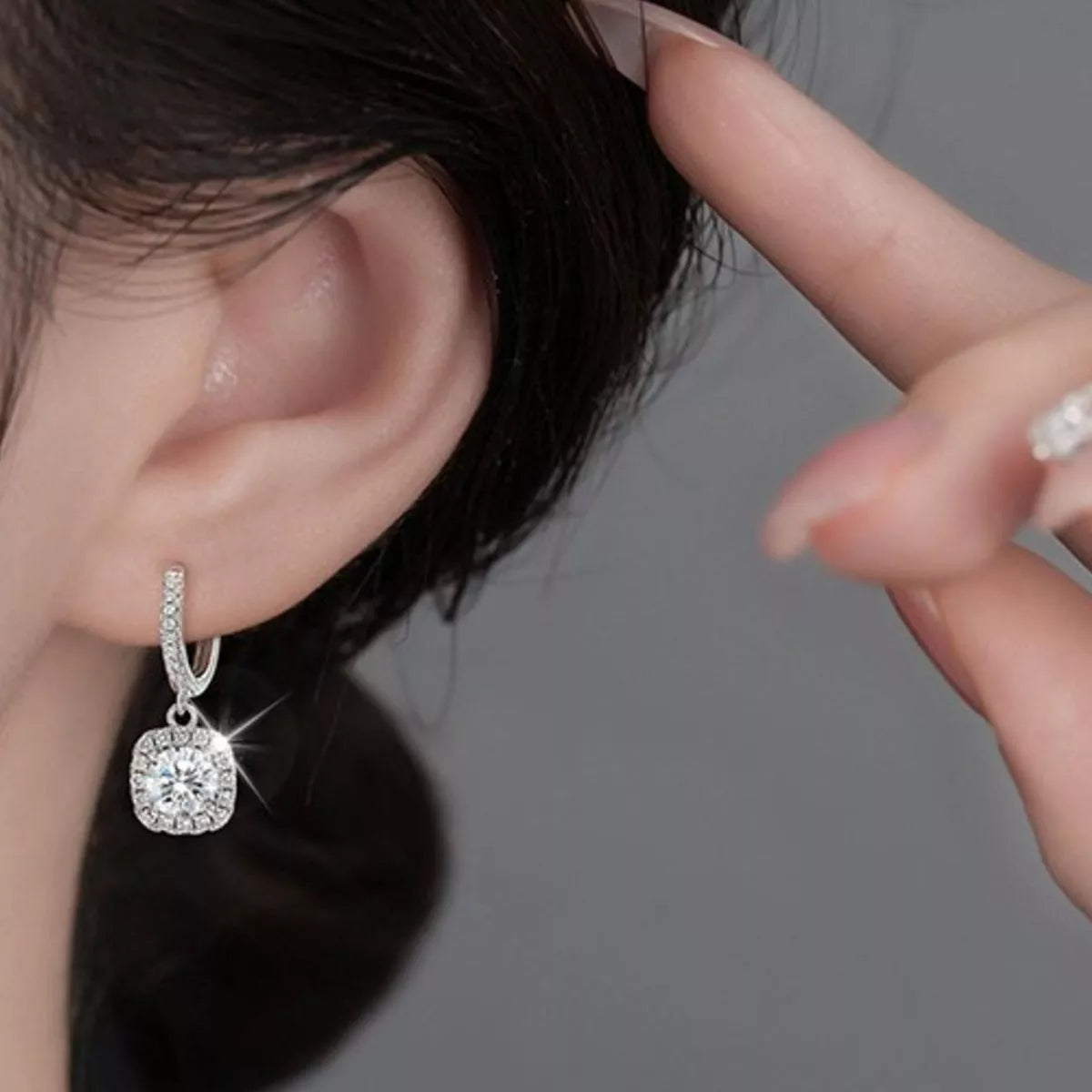 Silver-tone hoop earrings with square halo stone drops worn on a model