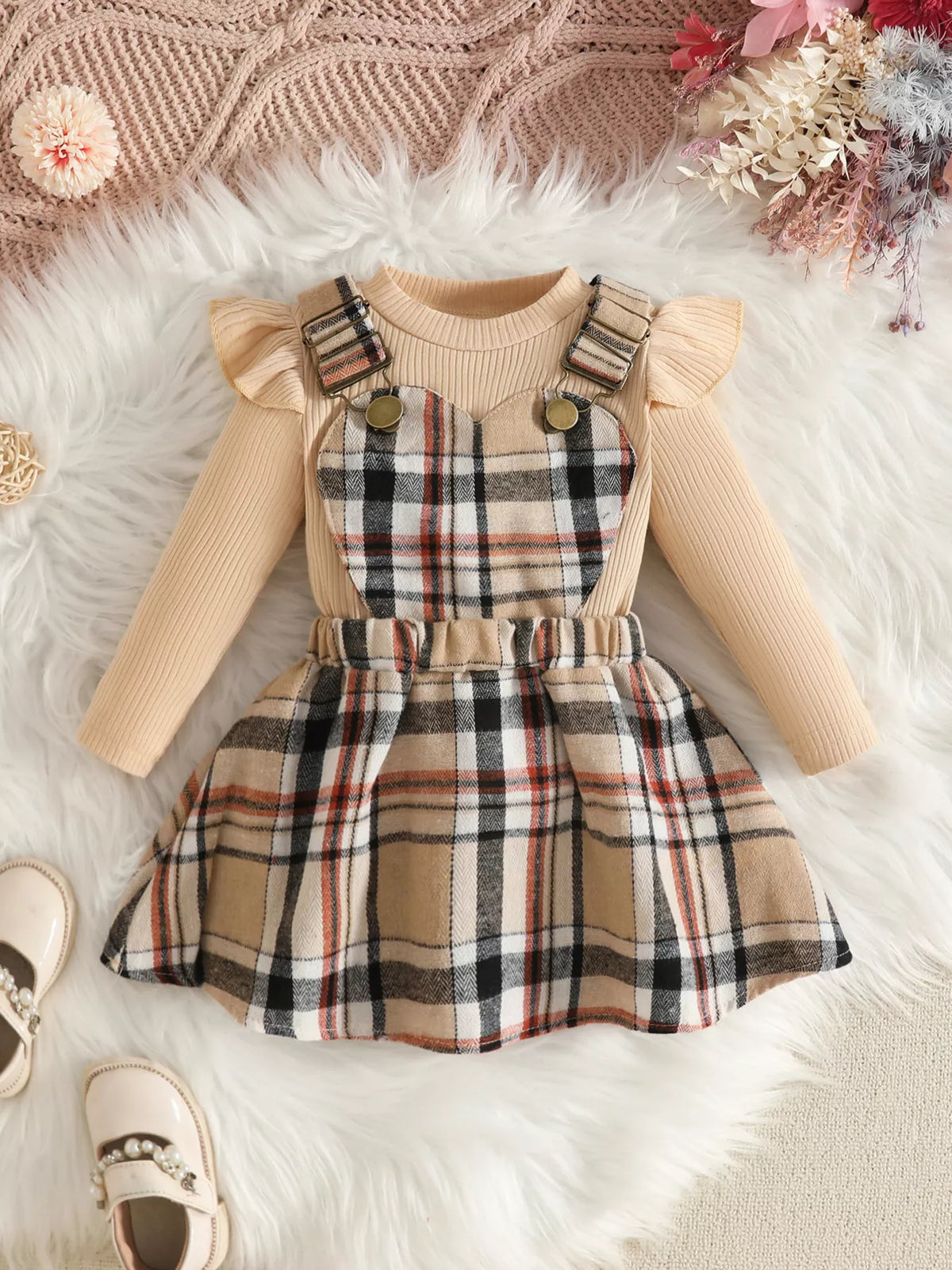 Cream ruffle-shoulder top paired with a beige plaid suspender skirt.