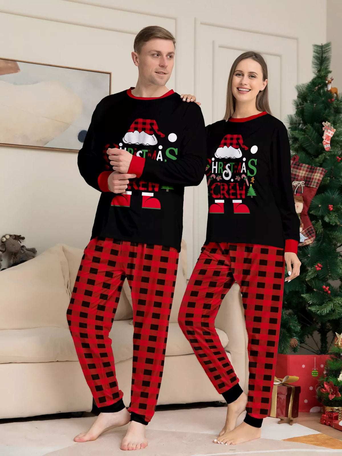 Adults wearing matching black Christmas graphic tops with red plaid pants.