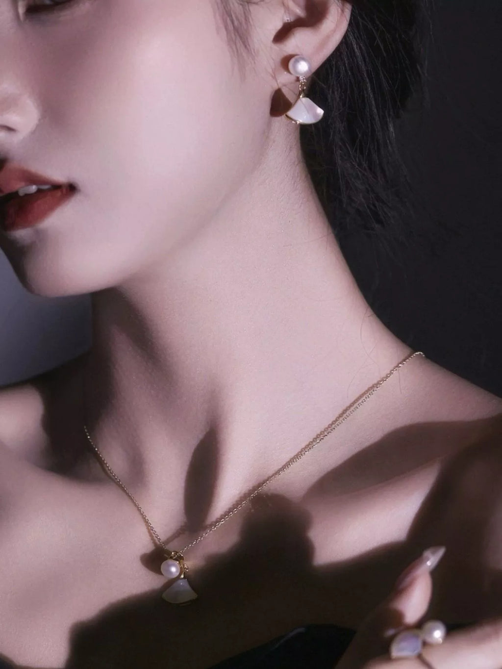Fan-shaped drop earrings with pearl-like beads and gold-tone edges worn on a model