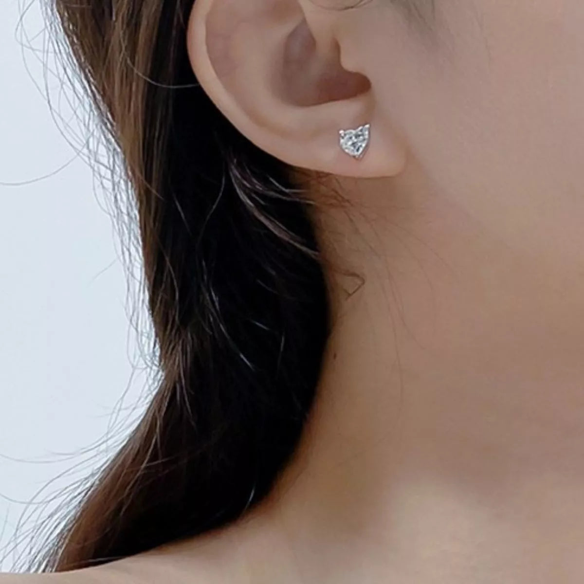 Silver-tone heart-shaped clear stone stud earrings worn on a model
