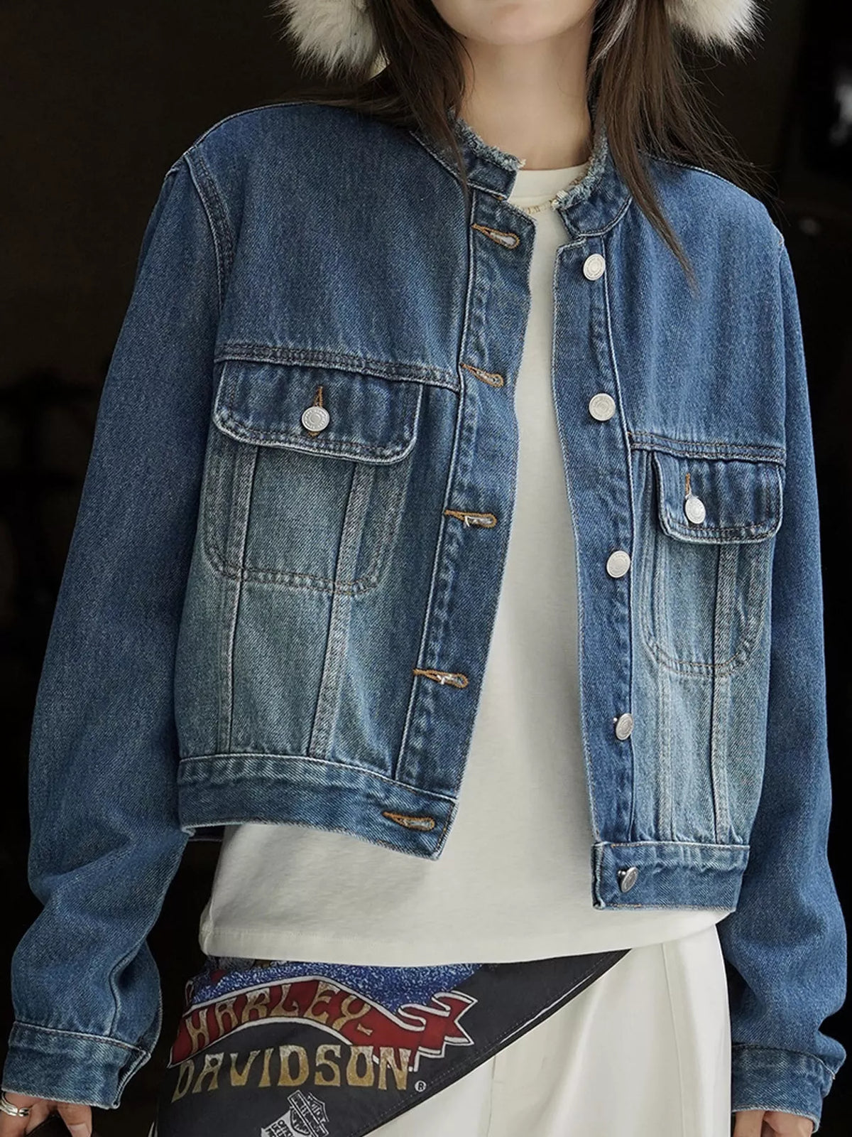 Blue cropped denim jacket with a round neckline and buttoned chest pockets.