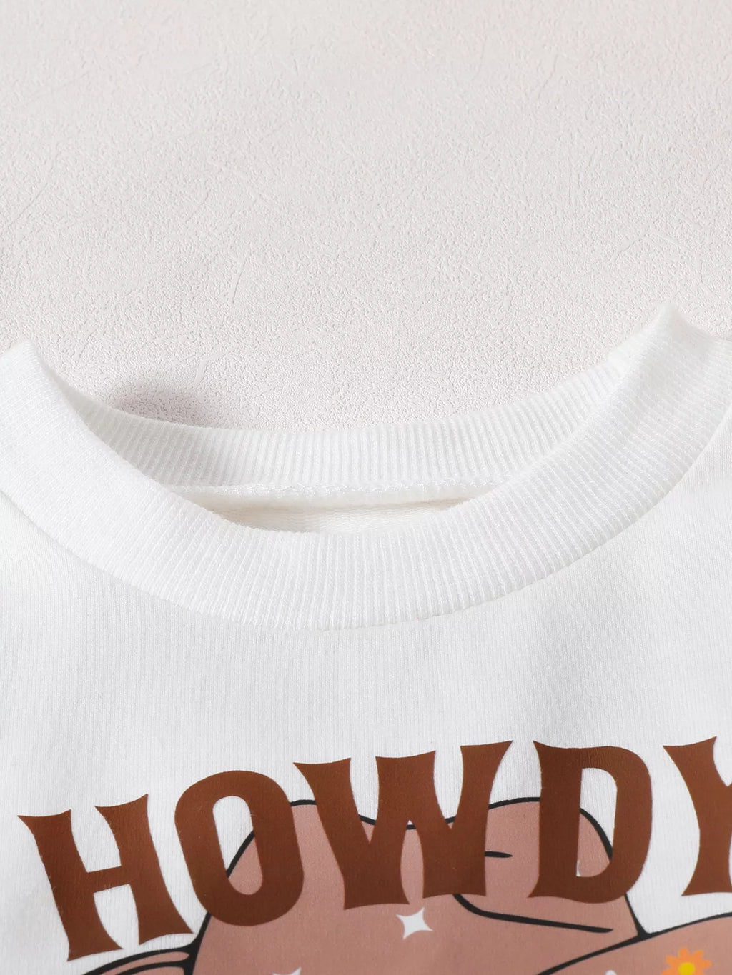 Close-up of the white top's ribbed neckline and Howdy lettering.