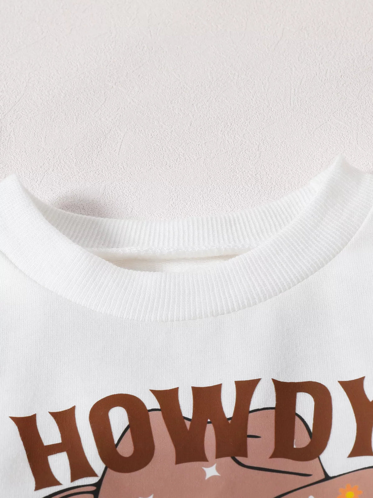 Close-up of the white top's ribbed neckline and Howdy lettering.
