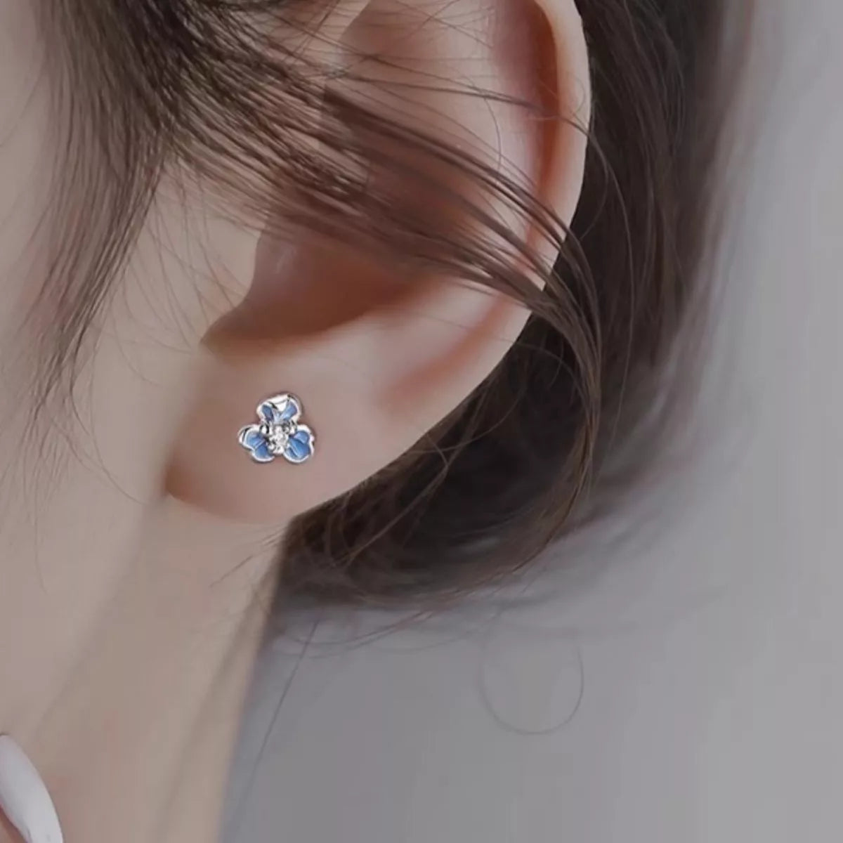 Silver-tone flower stud earrings with blue stones worn on a model