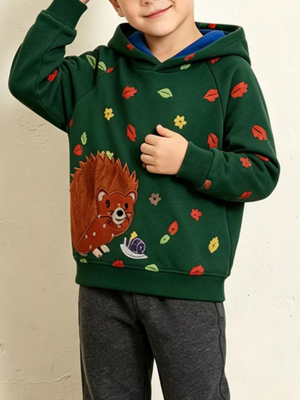 Children’s green hedgehog-print hoodie with contrasting blue hood lining worn by a child